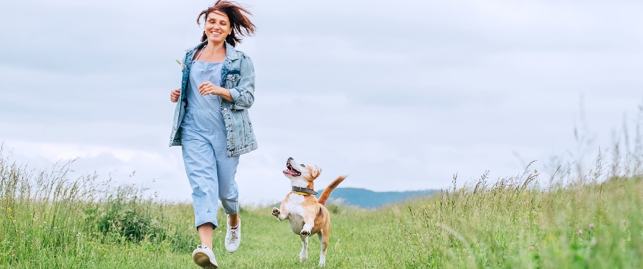 woman and her dog running through grass field