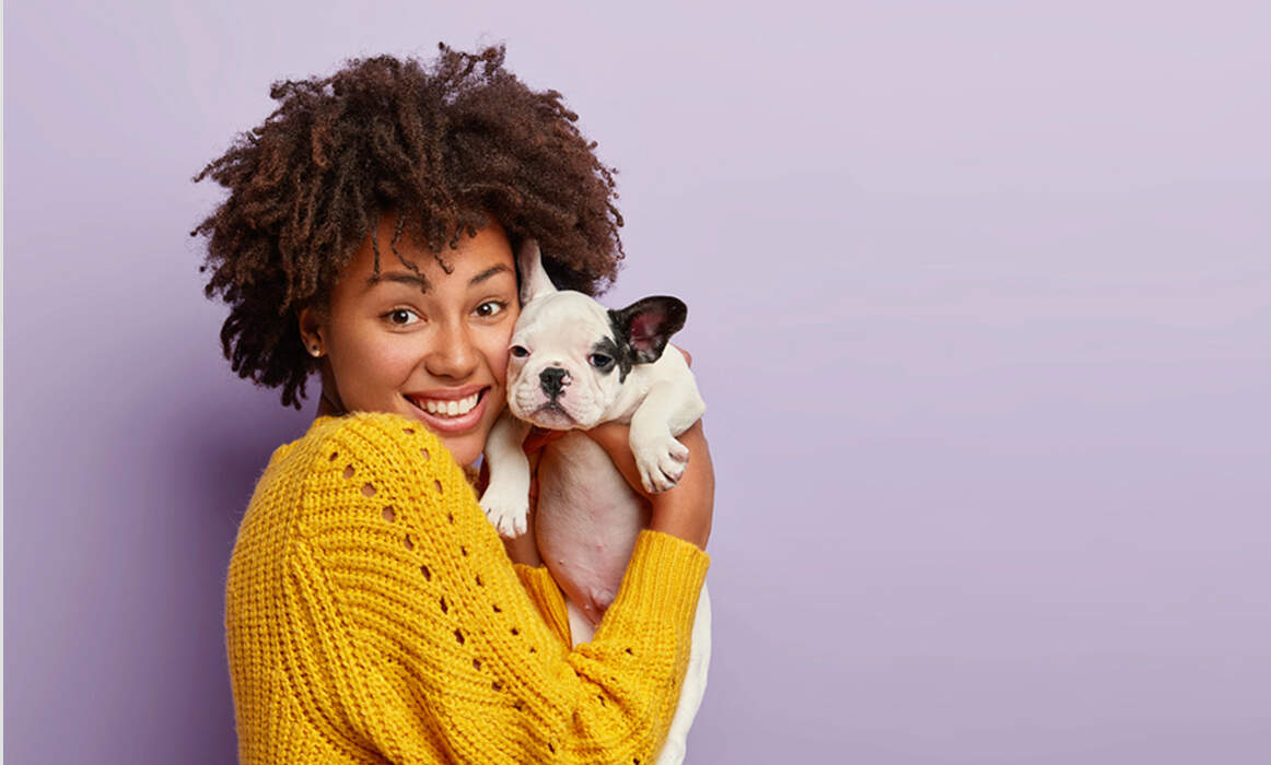 Lady wearing a yellow sweater holding their small dog.